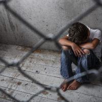 Depressed juvenile immigrant sitting alone behind a chain link fence