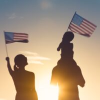 Patriotic man, woman, and child waving American flags in the air.