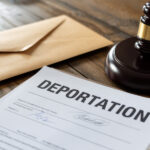 A deportation document lies on a wooden table with a brown envelope and a judge's gavel, conveying a serious and legal tone.